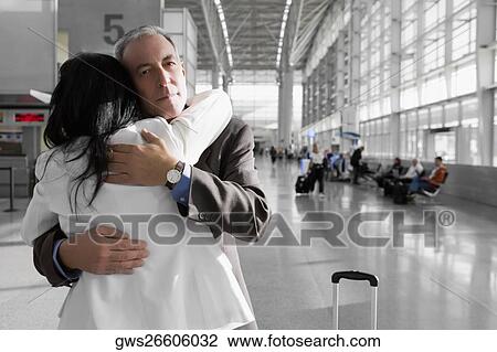 Stock Image - Businessman and a businesswoman hugging each other at an airport. Fotosearch