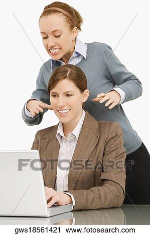 Businesswoman working on a laptop with her colleague try to strangle behind her View Large Photo Image Stock Image - Businesswoman working on a laptop with her colleague try to strangle behind her. Fotosearch