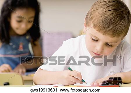Stock Image - Close-up of a boy drawing on a sheet of paper with a girl sitting behind him. Fotosearch