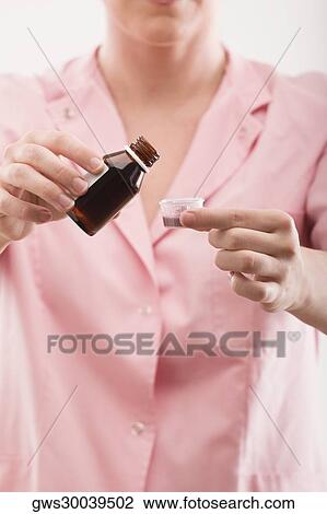 Stock Image - Close-up of a female nurse pouring syrup into a measuring cup. Fotosearch