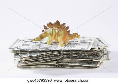 Stock Photograph - Close-up of a figurine of a dinosaur on a stack of US paper currency. Fotosearch