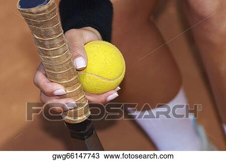 Stock Image - Close-up of a person's hand holding a tennis racket with a tennis ball. Fotosearch