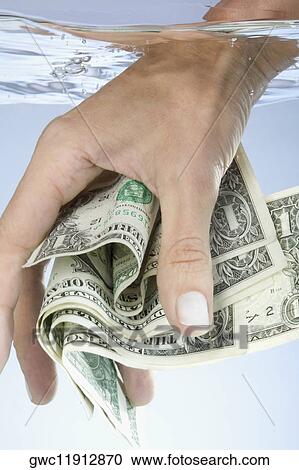 Stock Image - Close-up of a person's hand holding paper currency in water. Fotosearch