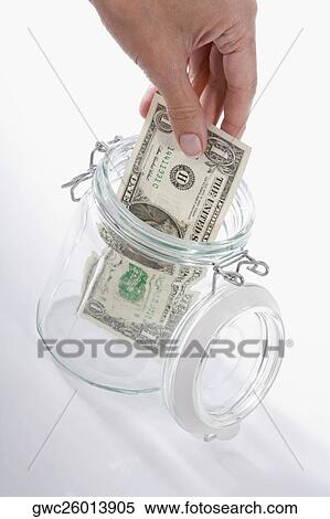 Stock Photography - Close-up of a person's hand picking a US dollar bill from a jar. Fotosearch