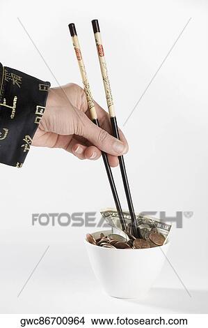 Picture - Close-up of a person's hand picking coins with chopsticks. Fotosearch
