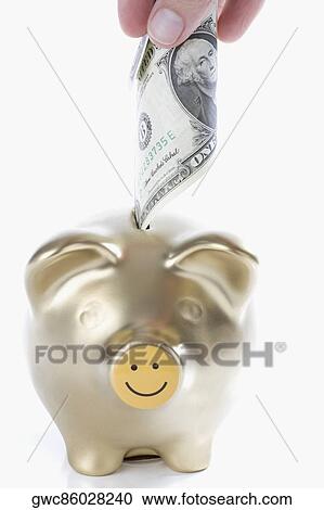 Stock Image - Close-up of a person's hand putting US paper currency into a piggy bank. Fotosearch