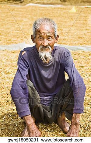 Stock Image - Close-up of a senior man crouching over rice grain, Zhigou, Shandong Province, China. Fotosearch