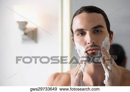 Stock Photo - Close-up of a young man applying shaving cream on his face. Fotosearch