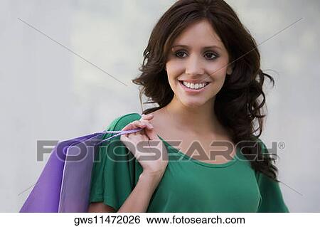 Close-up of a young woman carrying a shopping bag and smiling View Large Photo Image Stock Photograph - Close-up of a young woman carrying a shopping bag and smiling. Fotosearch