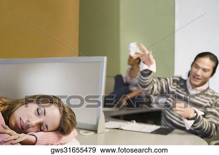 Stock Photo - Close-up of a young woman napping and a young man throwing a crumpled paper on her. Fotosearch