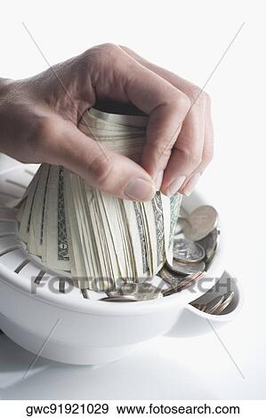 Stock Photo - Close-up of person's hand squeezing US dollar bills in a juicer. Fotosearch