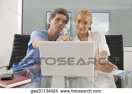 Female doctor and a male surgeon sitting in front of a laptop View Large Photo Image Picture - Female doctor and a male surgeon sitting in front of a laptop. Fotosearch