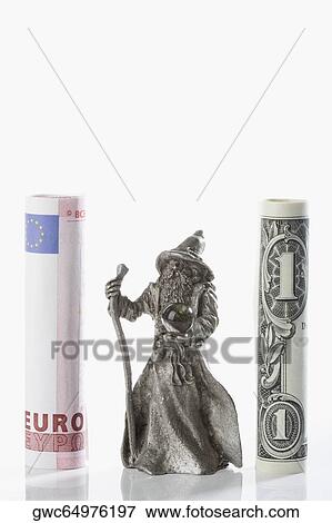 Stock Photo - Figurine of a fortune teller between rolls of European union euro note and US paper currency. Fotosearch