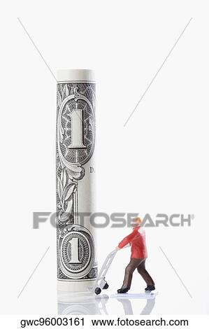 Stock Image - Figurine of a manual worker carrying a rolled up US paper currency on a push cart. Fotosearch