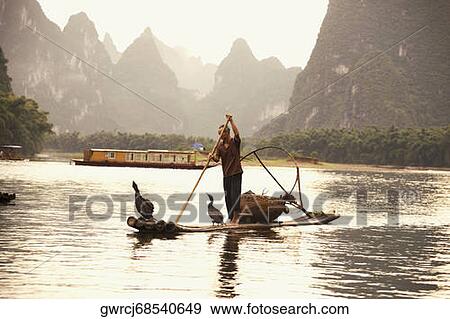 Fisherman on a wooden raft with a hill range in the background, Guilin Hills, XingPing, Yangshuo, Guangxi Province, China View Large Photo Image Stock Photo - Fisherman on a wooden raft with a hill range in the background, Guilin Hills, XingPing, Yangshuo, Guangxi Province, China. Fotosearch