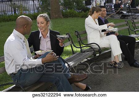 Picture - Four business executives having food on park benches. Fotosearch