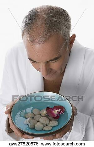 Stock Photograph - High angle view of a senior man holding a bowl of water with pebbles and floating flower. Fotosearch