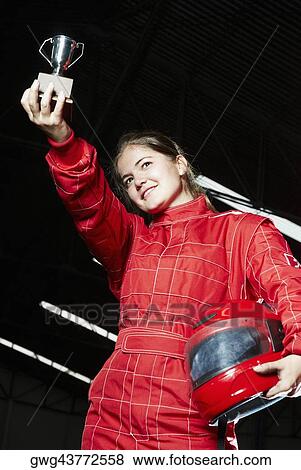 Stock Photo - Low angle view of a female go-cart racer holding a trophy and smiling. Fotosearch