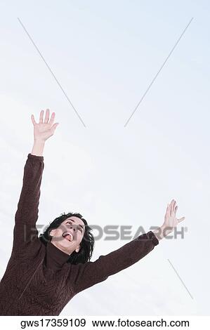 Stock Photo - Low angle view of a mature woman shouting with her arms raised. Fotosearch