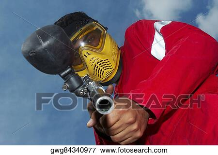 Stock Photo - Low angle view of a mid adult man aiming with a paintball gun. Fotosearch