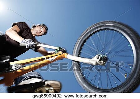 Stock Image - Low angle view of a young man performing a stunt on a bicycle. Fotosearch