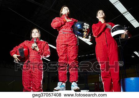 Stock Photo - Low angle view of three female go-cart racers standing on winners podium with their trophies. Fotosearch