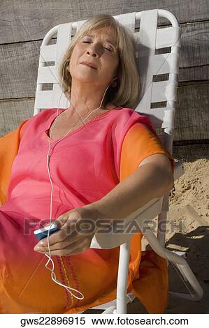 Stock Photography - Mature woman sitting on a chair and listening to an MP3 player. Fotosearch