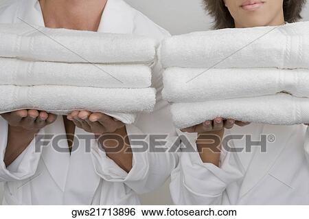 Stock Photograph - Mid section view of a mid adult man with a young woman holding stacks of folded towels. Fotosearch