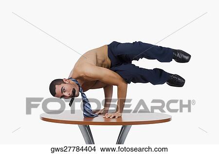 Picture - Portrait of a businessman doing a handstand on a table with a mobile phone in his mouth. Fotosearch