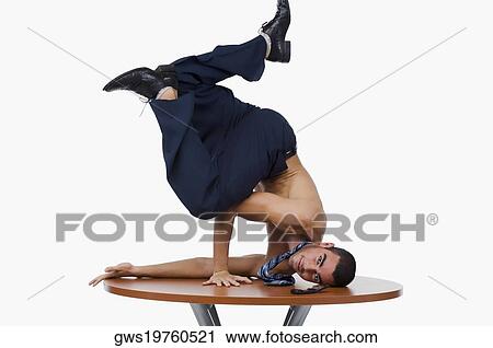 Stock Image - Portrait of a businessman doing a handstand on a table. Fotosearch