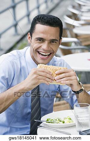 Stock Image - Portrait of a businessman eating a cheese sandwich and smiling. Fotosearch