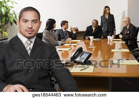 Stock Image - Portrait of a businessman smiling with other business executives in a board room. Fotosearch