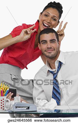 Stock Photograph - Portrait of a businesswoman gesturing rabbit ears behind a businessman and smiling. Fotosearch