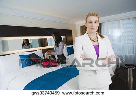 Portrait of a businesswoman standing with her arms crossed with another businesswoman packing her luggage View Large Photo Image Stock Photo - Portrait of a businesswoman standing with her arms crossed with another businesswoman packing her luggage. Fotosearch