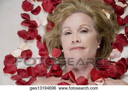 Stock Photograph - Portrait of a mature woman lying on a massage table with rose petals on her body. Fotosearch