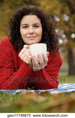 Portrait of a mid adult woman lying in a park and holding a coffee cup View Large Photo Image Stock Image - Portrait of a mid adult woman lying in a park and holding a coffee cup. Fotosearch