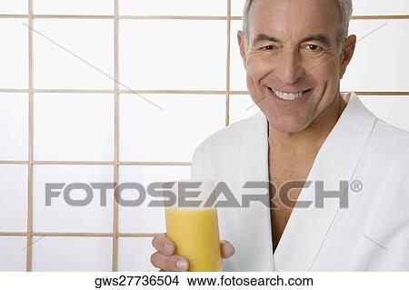 Picture - Portrait of a senior man holding a glass of orange juice and smiling. Fotosearch