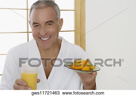 Stock Image - Portrait of a senior man holding a plate of oranges and a glass of orange juice. Fotosearch