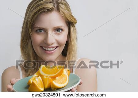 Stock Image - Portrait of a teenage girl holding a plate of oranges and smiling. Fotosearch