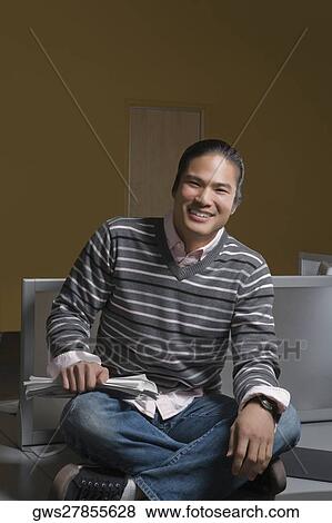 Portrait of a young man sitting in a computer lab and holding a book View Large Photo Image Stock Photo - Portrait of a young man sitting in a computer lab and holding a book. Fotosearch