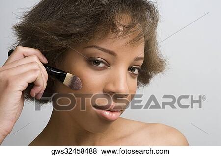 Portrait of a young woman applying blush on her cheek View Large Photo Image Stock Photo - Portrait of a young woman applying blush on her cheek. Fotosearch