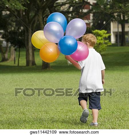 Stock Photo - Rear view of a boy holding balloons in a park. Fotosearch