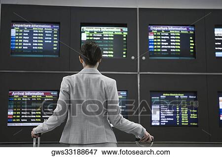 Stock Photo - Rear view of a businesswoman looking at arrival departure board at an airport. Fotosearch