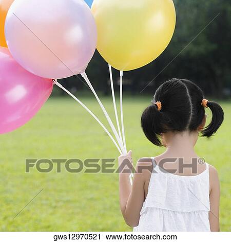 Rear view of a girl holding balloons in a park View Large Photo Image Stock Image - Rear view of a girl holding balloons in a park. Fotosearch