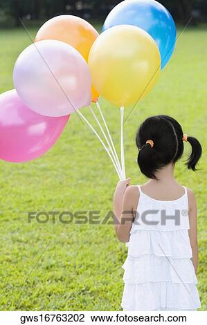 Stock Image - Rear view of a girl holding balloons in a park. Fotosearch