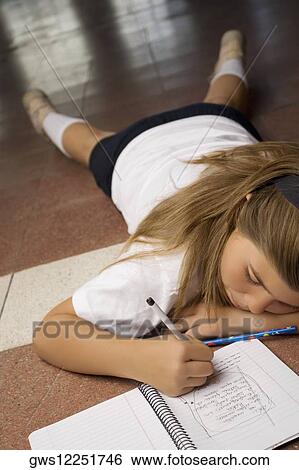 Stock Photograph - Schoolgirl lying on the floor and writing in a spiral notebook. Fotosearch