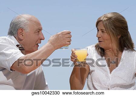 Senior couple toasting with glasses of juice and smiling View Large Photo Image Stock Image - Senior couple toasting with glasses of juice and smiling. Fotosearch