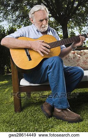 Stock Photo - Senior man sitting on a couch and playing a guitar. Fotosearch