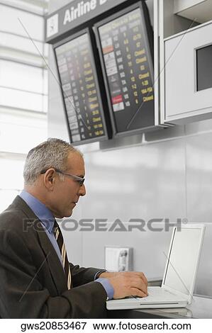 Stock Photo - Side profile of a businessman using a laptop at an airport check-in counter. Fotosearch