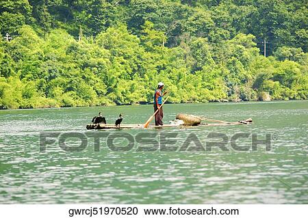 Stock Image - Side profile of a fisherman standing on a bamboo raft in a river, XingPing, Yangshuo, Guangxi Province, China. Fotosearch
